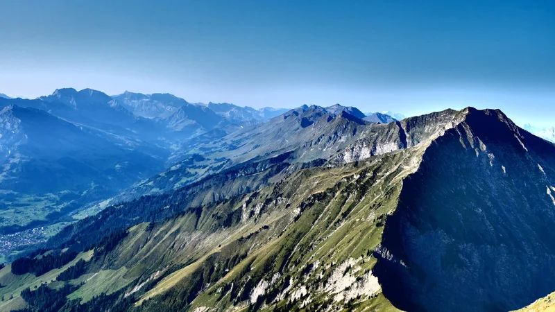 Blick über einen grünen und felsigen Berggrat auf weitere Gipfel.