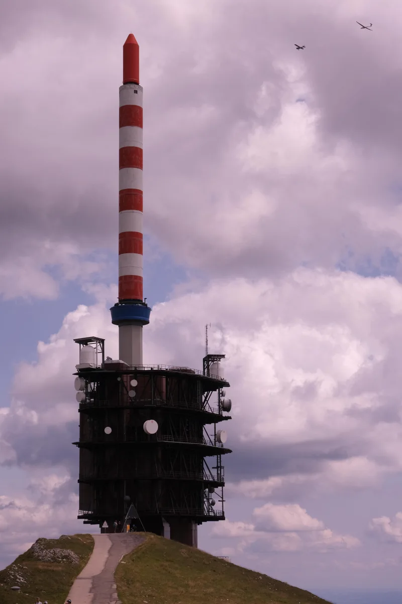 Ein rot-weiss gestreifter Sendemast auf einem dunklen Turm unter Wolken.