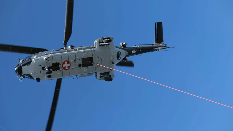 Ein Helikopter mit Schweizer Kreuz fliegt vor blauem Himmel.