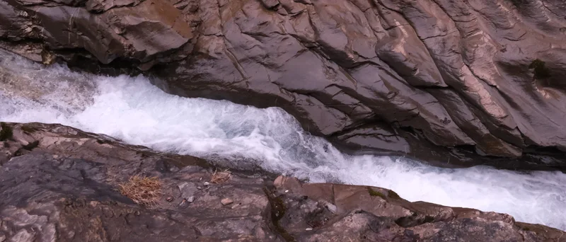 Weisses Wasser fliesst durch eine schmale Rinne zwischen dunklen Felsen.